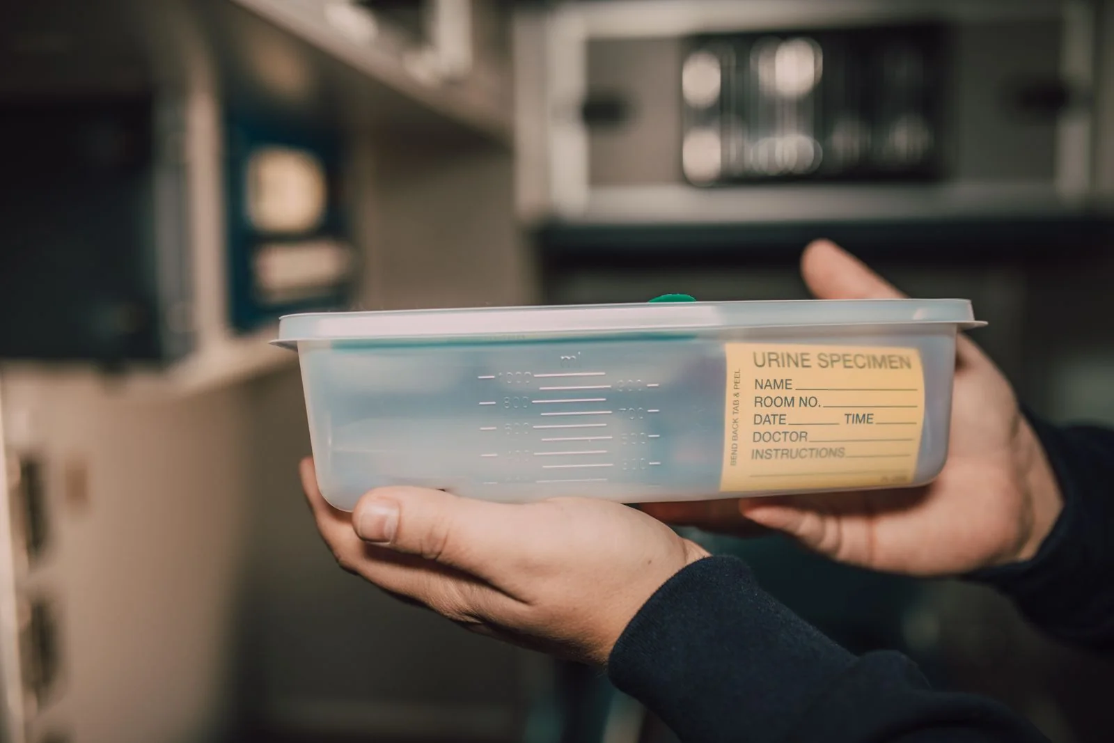 Urine specimen container held in someone’s hands. Stock photograph, not the specific Project Alliance kit.